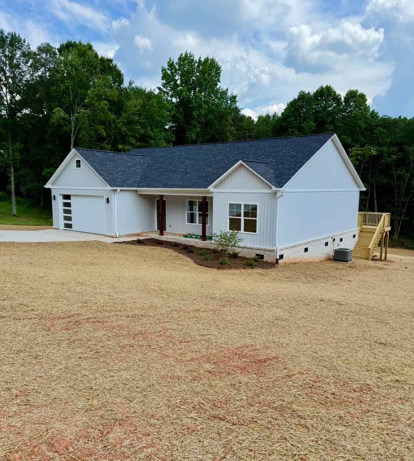 Completed white ranch home with attached garage, covered porch, and seeded yard